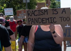 Protester with sign that says, Racism is a pandemic too